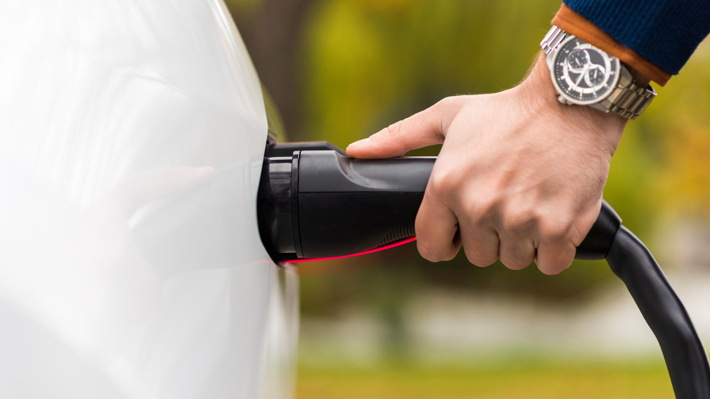 close view man plugging charger into electric car charging port E3 Lithium to Present at the Bloor Street Capital Virtual Battery Metals Conference on November 10